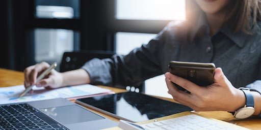 Woman looking at phone while seated at a desk using CXT Software.